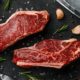 two steaks on a cutting board next to garlic, garlic, and a knife