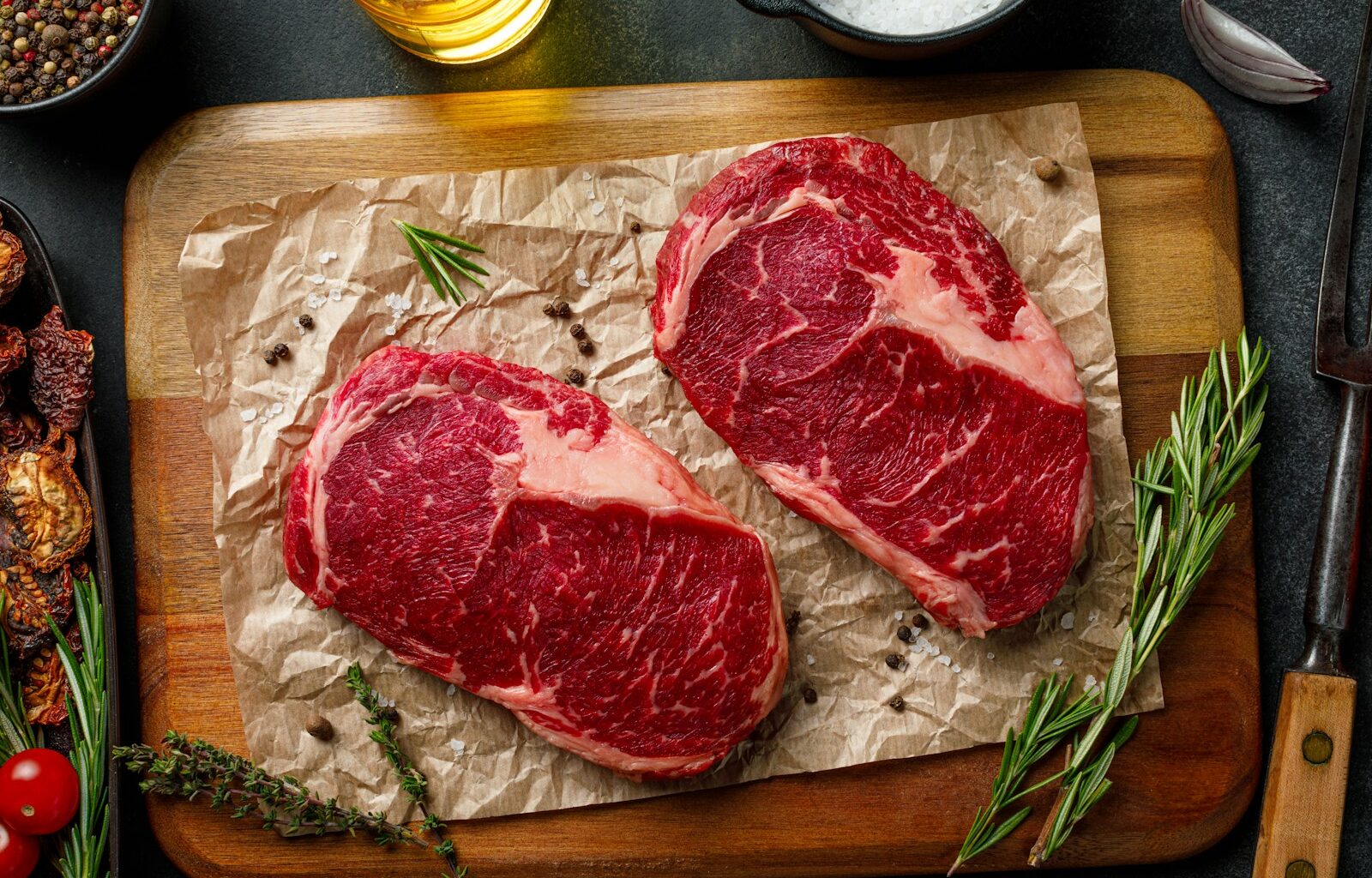 two steaks on a cutting board with herbs and spices