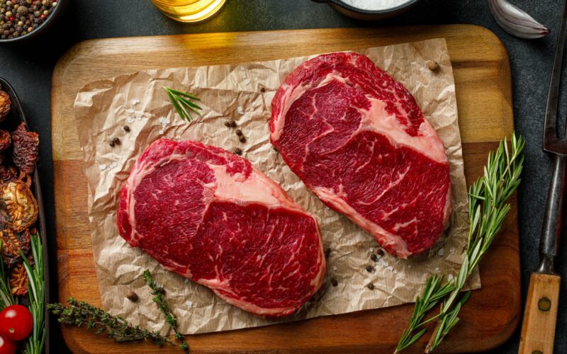 two steaks on a cutting board with herbs and spices